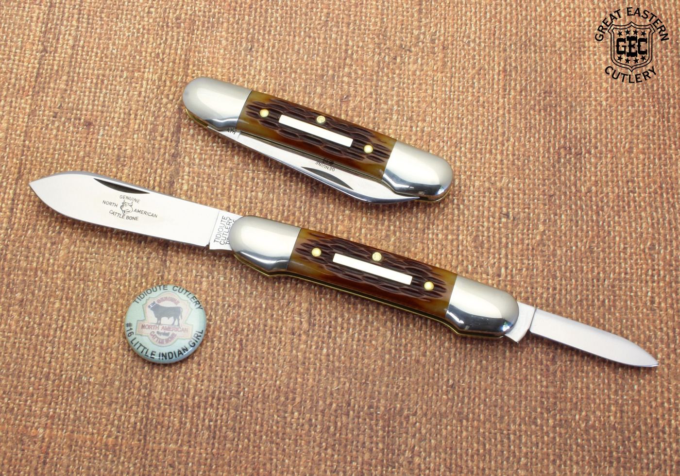 Two Tidioute Cutlery #16 slipjoint pocketknives with jigged bone handles and polished steel bolsters, photographed on burlap beside a Little Indian Girl pattern pin